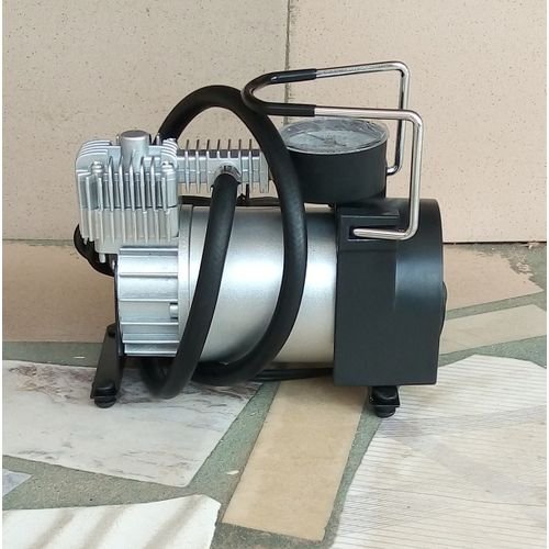 12 V portable metal tire inflator air compressor with gauge and hose on white background.
